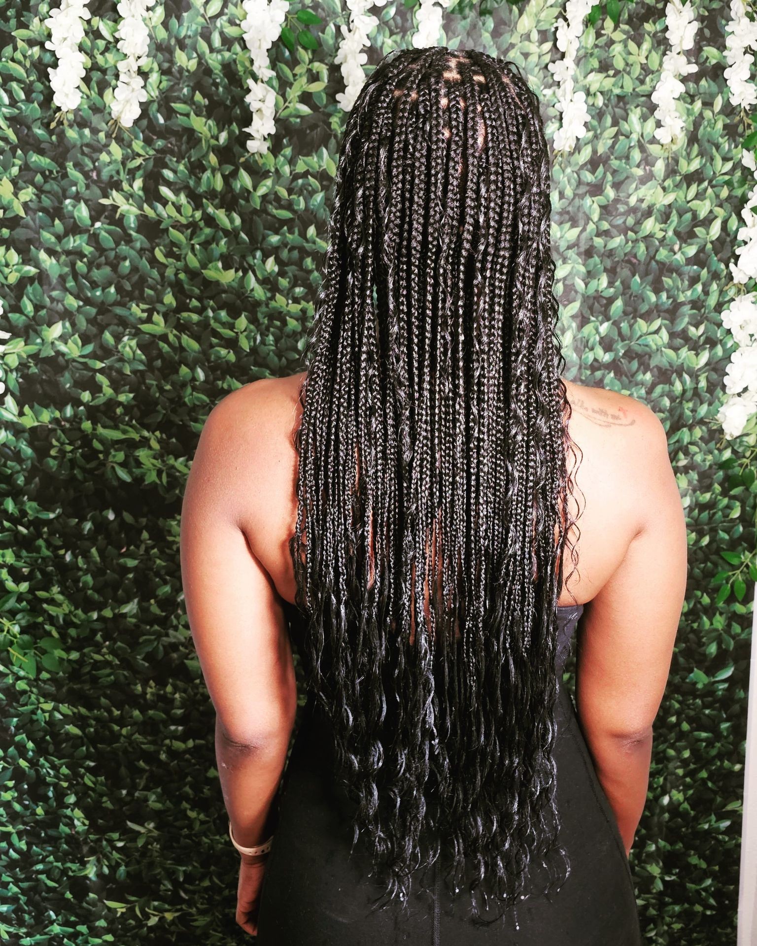 Person with long braided hair facing a leafy green background.